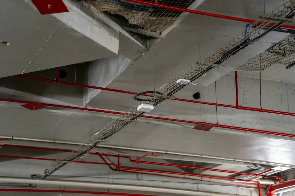 Red fire sprinkler pipes and cable trays below a concrete ceiling