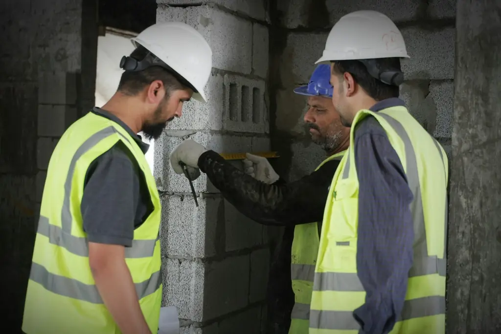 Site engineers in hard hats measuring a newly built block wall